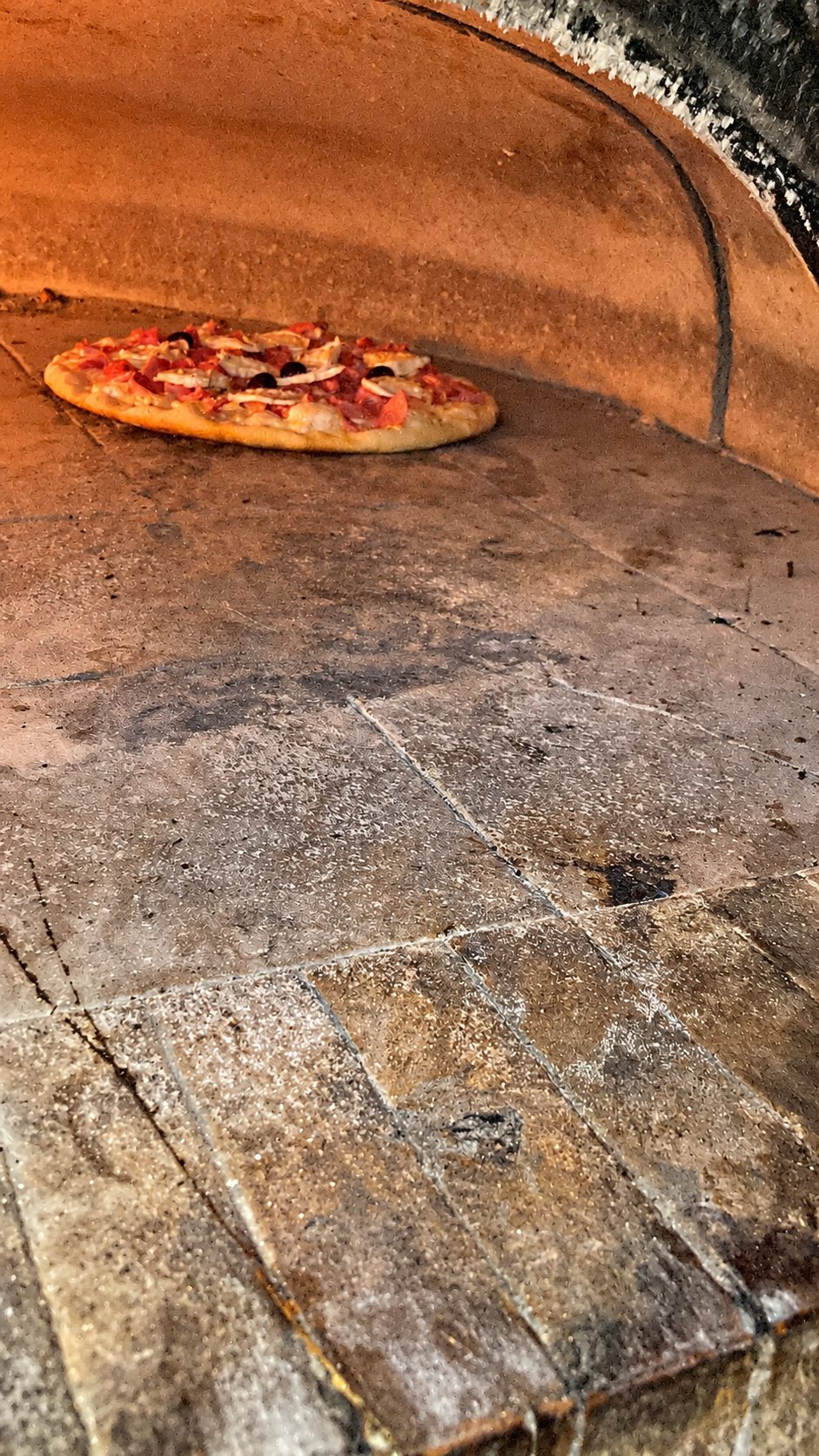 Pizza posée sur la sole en pierre d’un four voûté