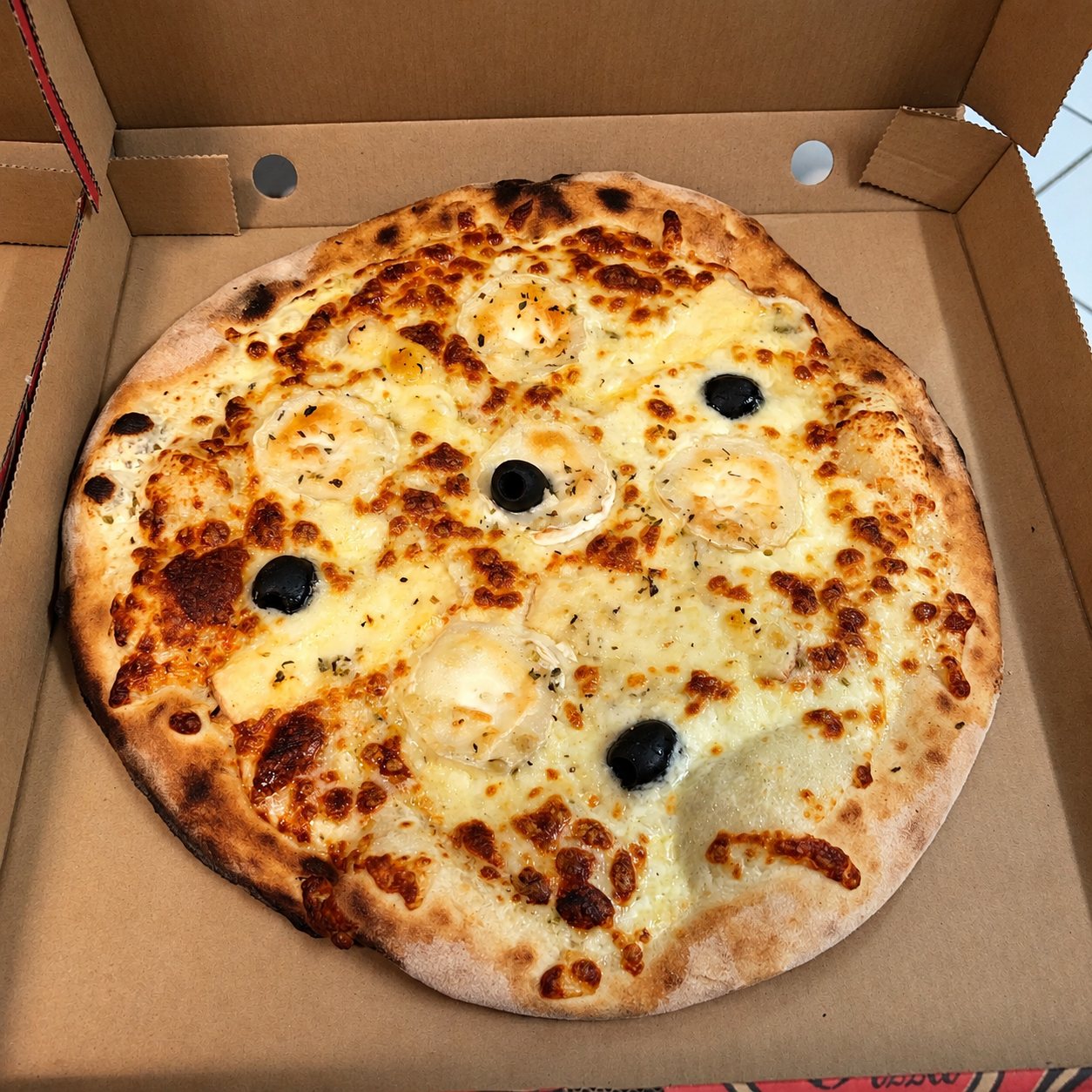 Pizza au fromage gratiné et aux olives noires dans son carton