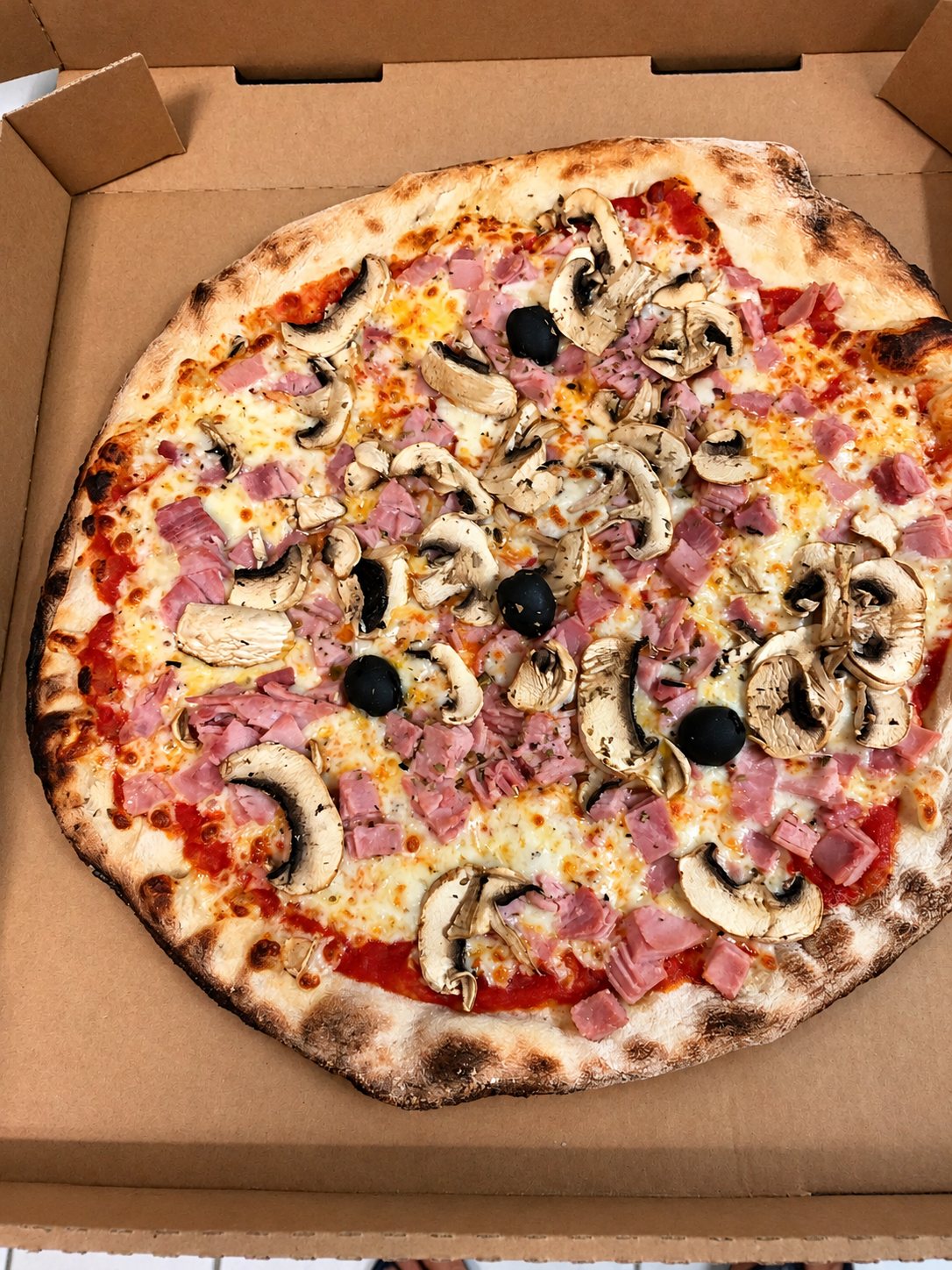 Pizza au jambon, champignons et olives noires dans son carton