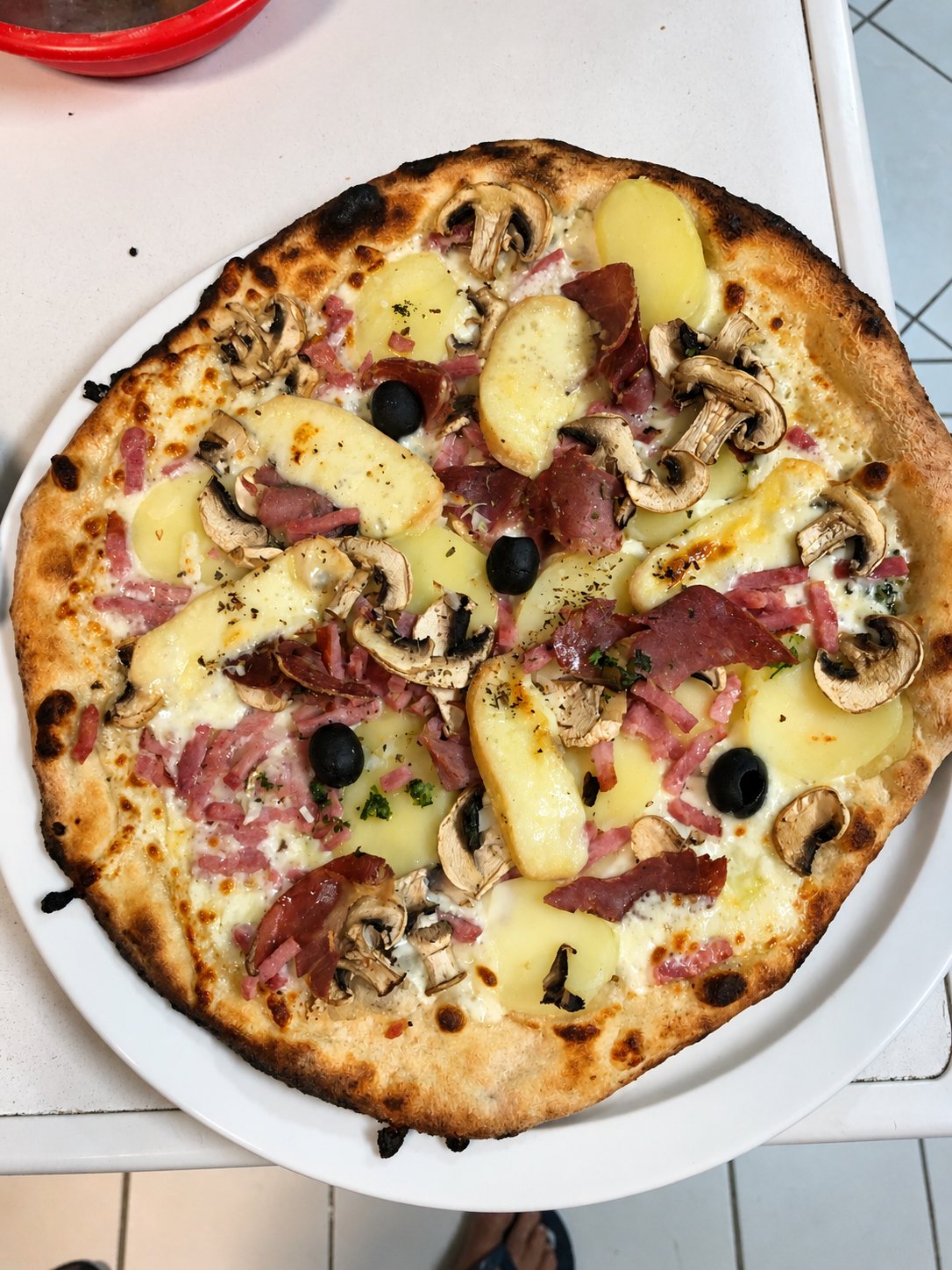 Pizza aux pommes de terre, jambon cru, champignons et olives sur une assiette