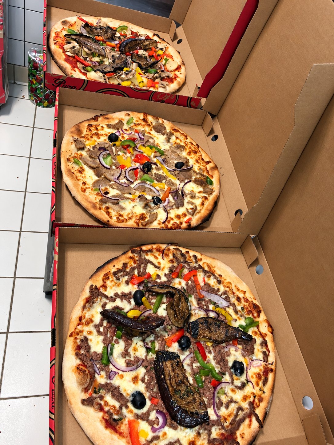 Trois pizzas garnies dans leurs cartons ouverts, empilés les uns sur les autres